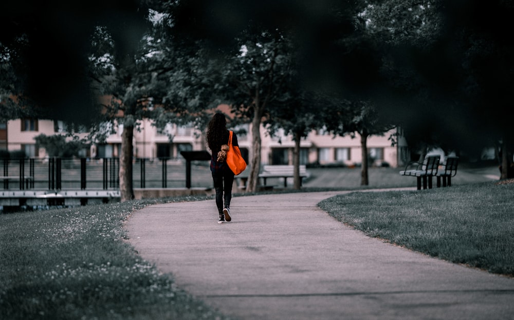 a woman walking down a sidewalk carrying a bright orange purse