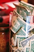 a glass filled with lots of money sitting on top of a table