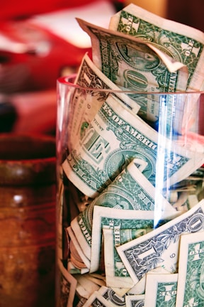 a glass filled with lots of money sitting on top of a table