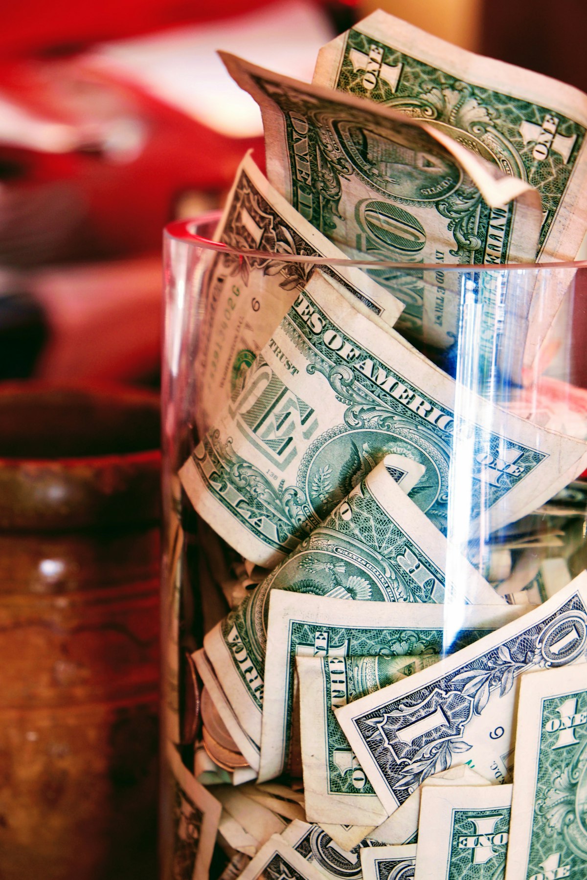A glass jar overflowing with one-dollar bills on a table, the saving and money-as-tangible-object register
