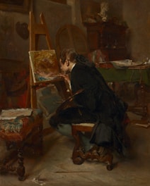 A person seated in an art studio, deeply focused on painting a canvas placed on an easel. The room is dimly lit, adding a warm, contemplative atmosphere. Surrounding the artist are various artistic tools and furniture, including a decorative stool, a table with papers, and a wooden cabinet. A bust sculpture is visible in the background, suggesting an inspirational setting.