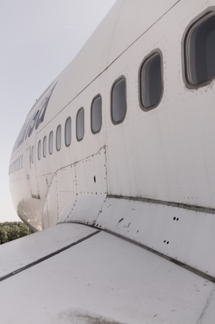 A detailed view of the side of an airplane, emphasizing the windows and riveted metal fuselage. The angle captures the curvature and texture of the aircraft, with some wear and tear visible on the surface.