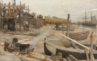 A detailed scene of a shipyard with workers actively engaged in various tasks. Wooden structures and scaffolding are prominently visible, with the hull of a ship under construction. Several boats and wooden planks are scattered around the area. Workers are seen in different positions, some building while others tend to smaller tasks like working the fire in the foreground. In the background, ships are anchored along the water.