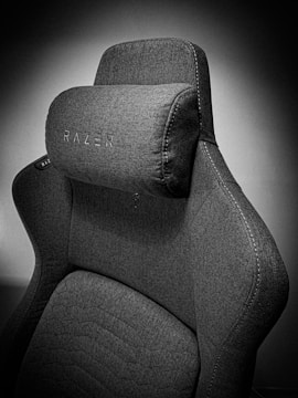 A high-quality, fabric gaming chair featuring ergonomic design and enhanced comfort. The chair has a distinct headrest with visible stitching, embossed branding, and a modern aesthetic.