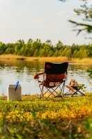 A sleek, foldable camping chair set up beside a tranquil lake at sunset.