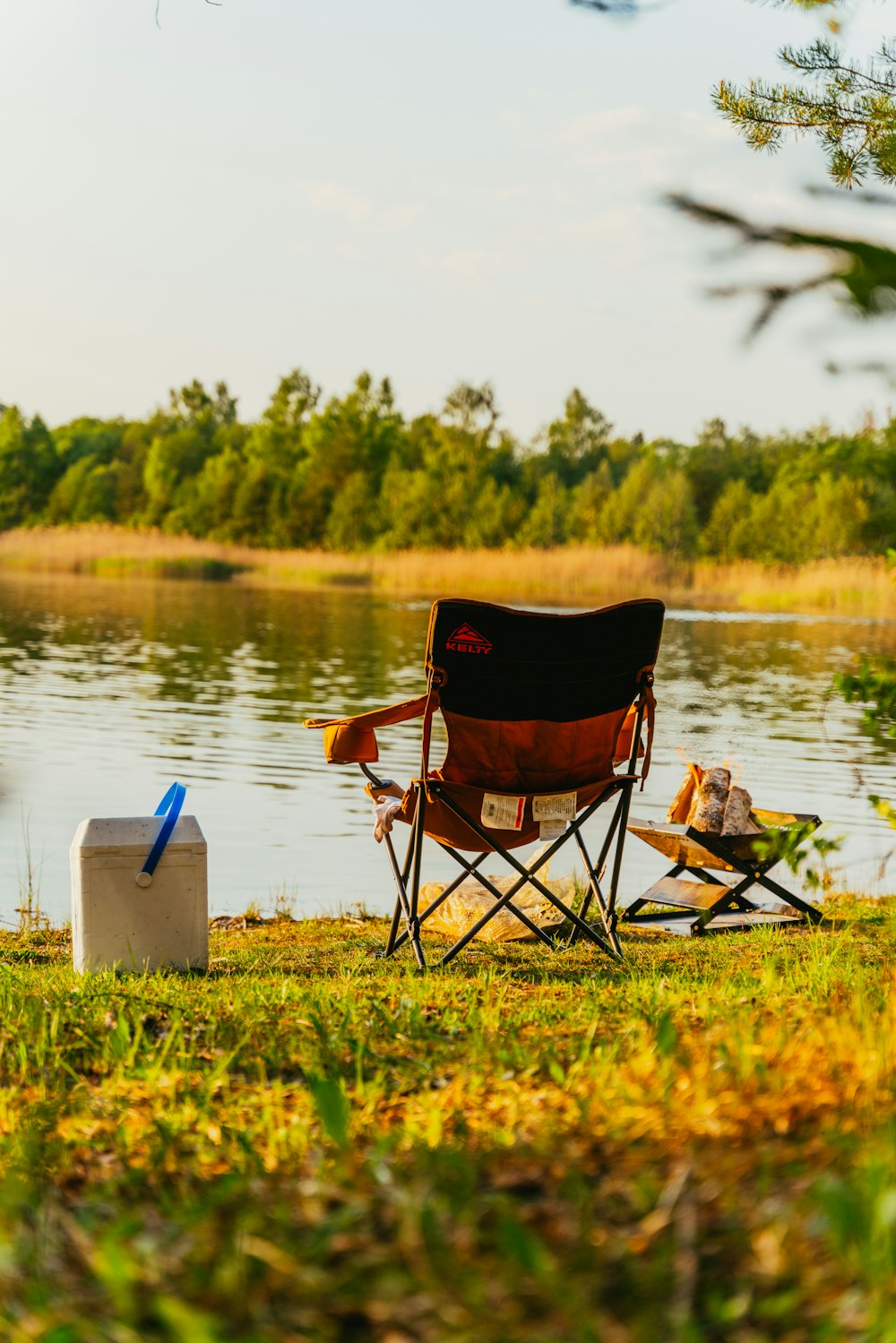 a chair and a cooler sitting on the shore of a lake