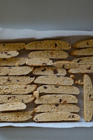 A tray of freshly baked biscotti arranged in rows on parchment paper. The biscotti are golden brown with visible pieces of dried fruit and nuts.