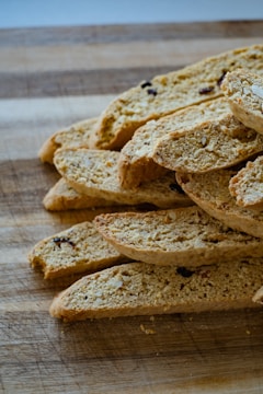 A stack of sliced biscotti placed on a wooden cutting board. The biscotti have a golden-brown color with visible nuts and dried fruit embedded within. The texture appears crunchy and crumbly.