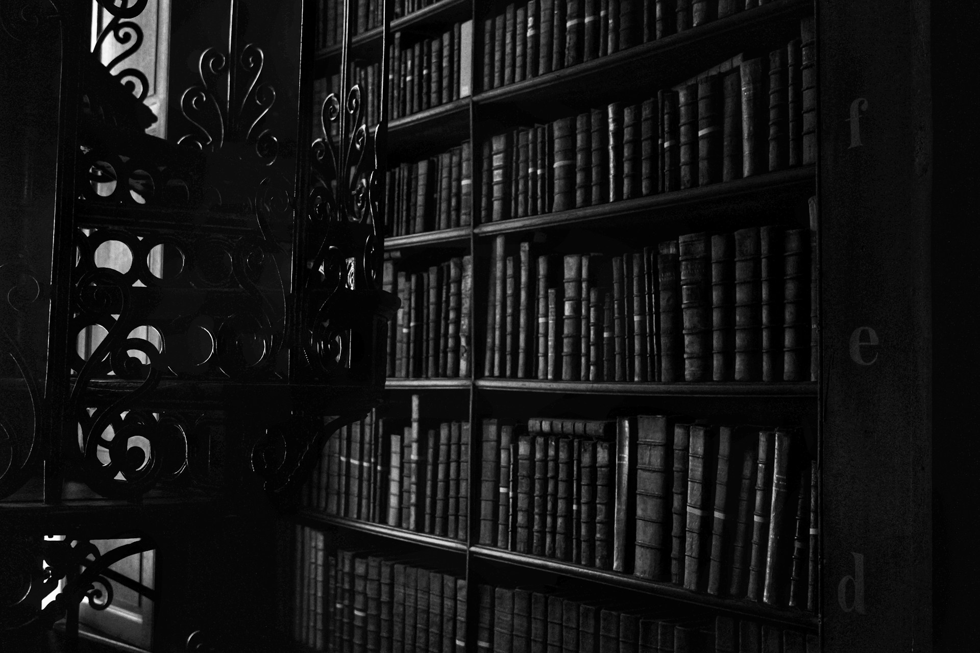 A shadowy library room filled with ancient, leather-bound books and dim candlelight casting flickering shadows on the walls.