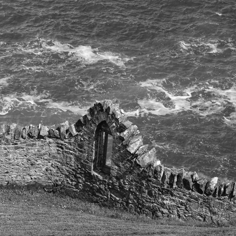 a black and white photo of a stone wall by the ocean