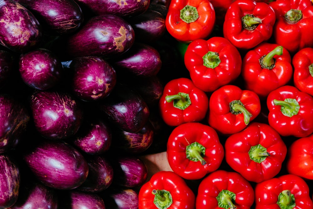 a pile of red peppers next to a pile of purple eggplant