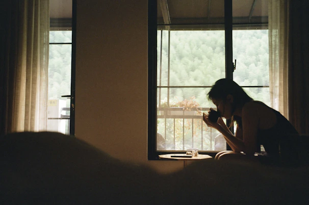 A serene woman sitting peacefully in a sunlit room, journaling with a cup of herbal tea nearby.