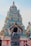 A person with folded hands is facing a colorful, intricately decorated Hindu temple. The temple is adorned with various statues and sculptures, showcasing detailed artistic craftsmanship.