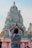 A person with folded hands is facing a colorful, intricately decorated Hindu temple. The temple is adorned with various statues and sculptures, showcasing detailed artistic craftsmanship.