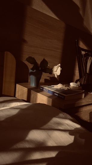 A bedroom corner with soft linens, a wooden nightstand, and a small vase of fresh flowers catching morning light.