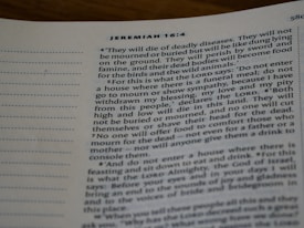 A close-up photograph of a page from the Bible, specifically Jeremiah 16:4. The text is printed in a serif font on white paper. The verses discuss themes of death and mourning.