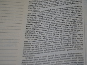 A close-up view of a page from a Bible, featuring printed text which speaks about divine retribution and behaviors of ancestors. The paper is slightly yellowed, and there are visible horizontal lines in the margins.