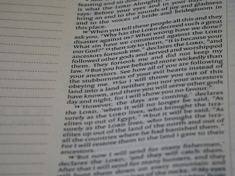 A close-up view of a page from a Bible, featuring printed text which speaks about divine retribution and behaviors of ancestors. The paper is slightly yellowed, and there are visible horizontal lines in the margins.