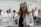 A woman wearing a virtual reality headset and holding controllers stands in a laboratory setting. She is dressed in a white lab coat and is surrounded by several people who are also in lab attire. Anatomical models are visible in the background, suggesting a medical or educational environment.