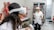 Two individuals wearing virtual reality headsets and holding controllers are inside a room filled with anatomical models and medical displays. Various anatomical figures, including muscles, organs, and skeletons, are visible. The individuals are dressed in lab coats, suggesting a scientific or educational setting.