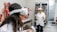 Two individuals wearing virtual reality headsets and holding controllers are inside a room filled with anatomical models and medical displays. Various anatomical figures, including muscles, organs, and skeletons, are visible. The individuals are dressed in lab coats, suggesting a scientific or educational setting.