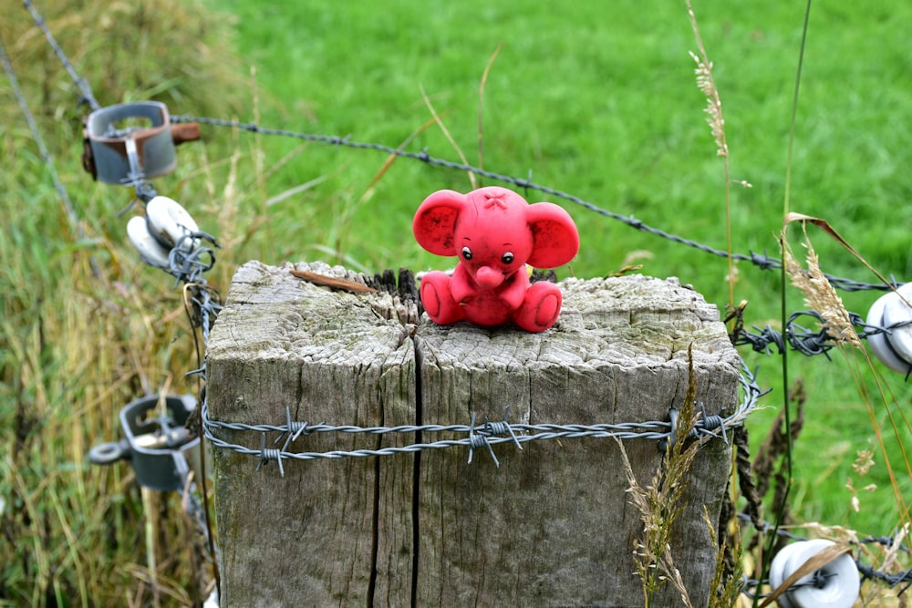 a red teddy bear sitting on top of a wooden post