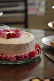 Close-up of a pink frosted cake with delicate white floral decorations on a wooden table.