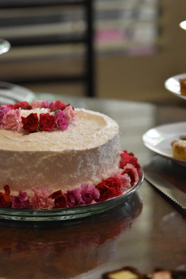 A close-up of a beautifully frosted vanilla cake with delicate pink rose decorations on a rustic wooden table
