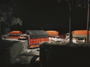 A gritty night-time garage scene with heavy trucks lined up under harsh industrial lighting.