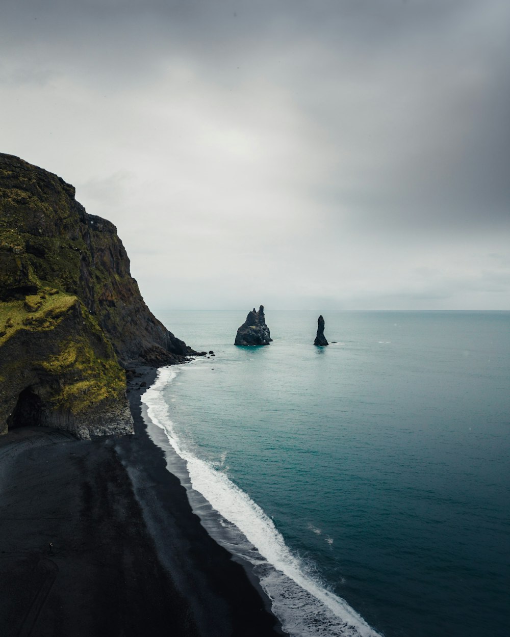 a black sand beach with a rock outcropping in the distance