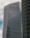 A modern high-rise building with reflective glass windows and the KPMG logo near the top. The structure features sleek, vertical lines and a mix of metal and glass materials. Another building with a curved façade is partially visible on the right side.