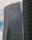 A modern high-rise building with reflective glass windows and the KPMG logo near the top. The structure features sleek, vertical lines and a mix of metal and glass materials. Another building with a curved façade is partially visible on the right side.