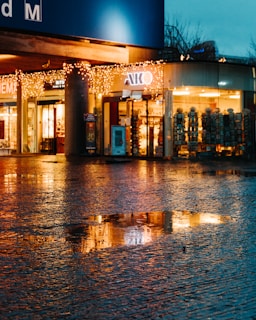 A serene street scene at dusk with warm light spilling from shop windows.
