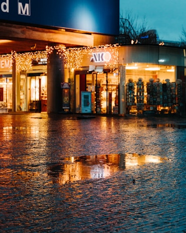 A serene street scene at dusk with warm light spilling from shop windows.