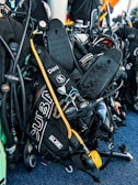 A collection of scuba diving equipment, including flippers, breathing regulators, air cylinders, and gauges, is arranged on a textured blue surface. The gear has various labels and branding, including 'Scubapro' and 'Oceanic.'