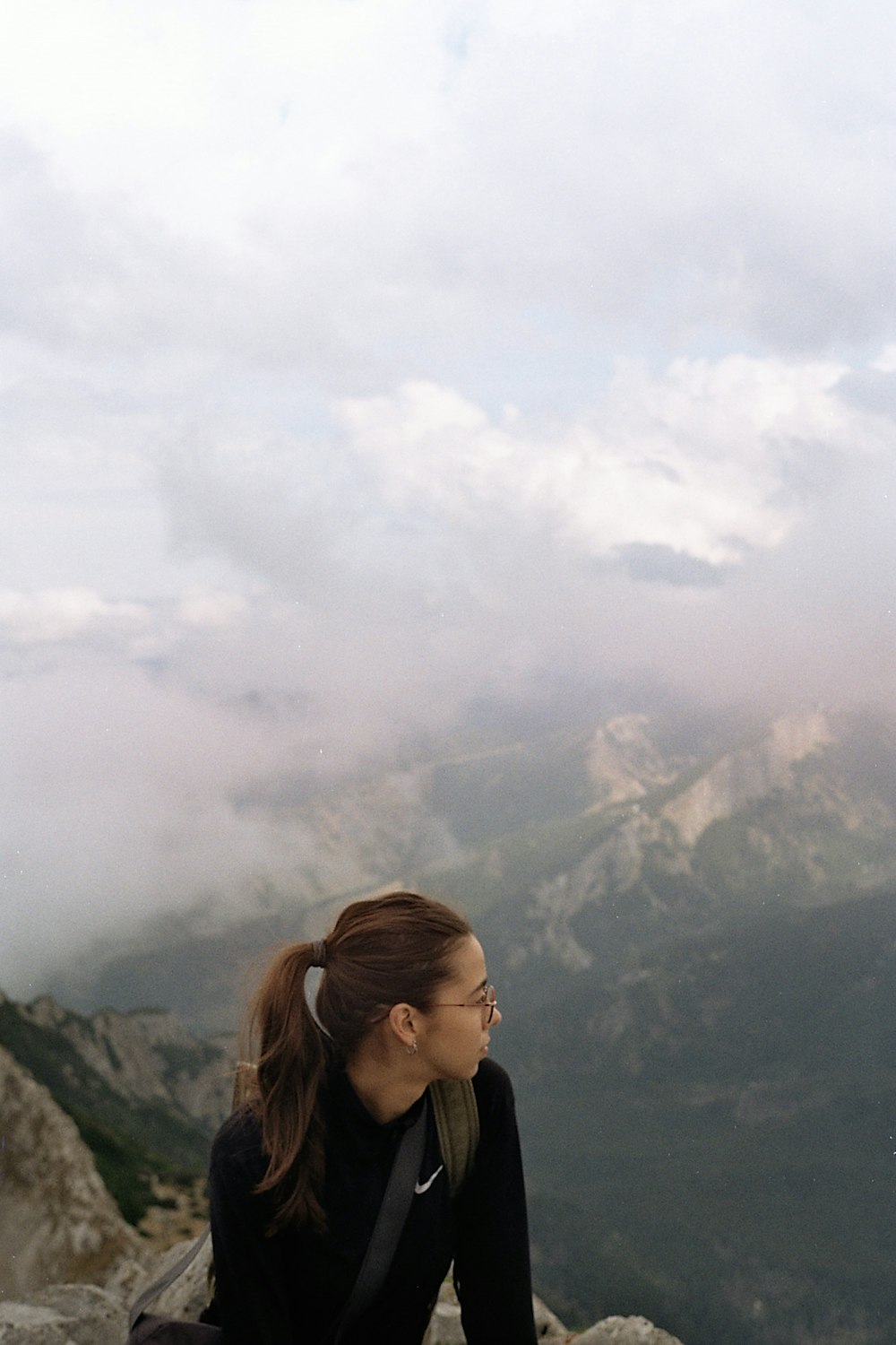 a woman sitting on top of a mountain with a sky background