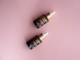 Close-up of a sleek serum bottle with glossy pink accents on a soft blush background.