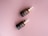 Two brown dropper bottles with golden caps are placed on a soft pink background. The bottles are labeled with a text indicating they are a serum product.