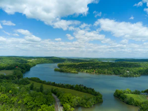 An aerial view of a serene river winding through a floodplain, bordered by lush greenery under a clear blue sky.