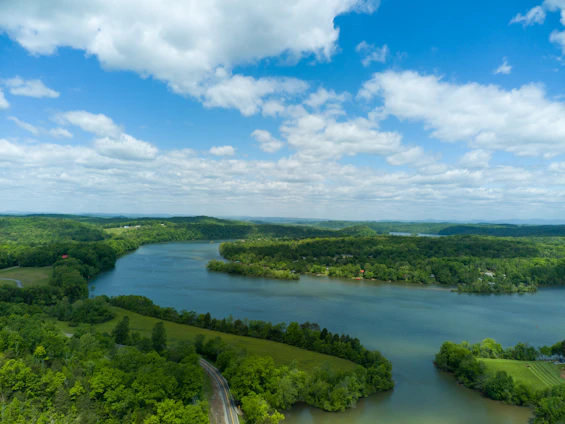 An aerial view of a serene river winding through a floodplain, bordered by lush greenery under a clear blue sky.