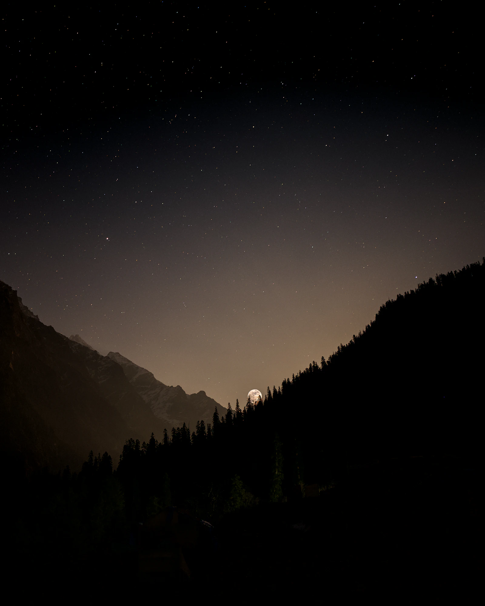 A full moon rising over a mountain range at dusk