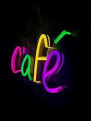 A vibrant neon box sign glowing brightly outside a cozy cafe at night.