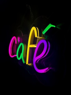 Brightly glowing neon sign displaying the word 'cafe' with letters in various colors against a dark background.