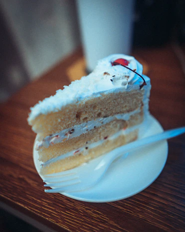 A slice of layered vanilla and strawberry cake with creamy frosting on a delicate plate.