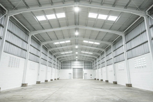 Nave industrial vacía de estructura metálica blanca iluminada de forma uniforme por luminarias de techo, escenario del marketing para empresas de eficiencia energética