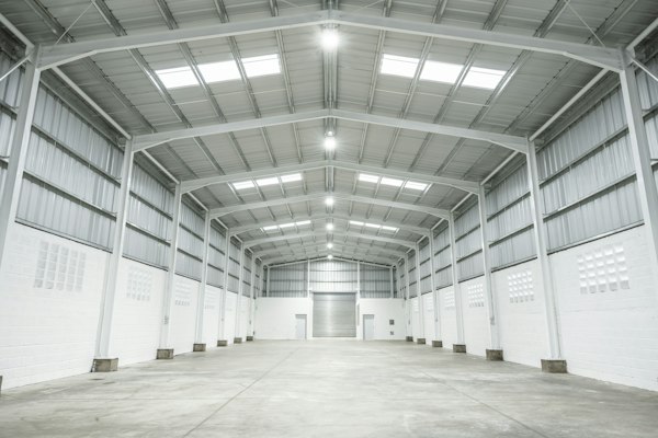 Nave industrial vacía de estructura metálica blanca iluminada de forma uniforme por luminarias de techo, escenario del marketing para empresas de eficiencia energética