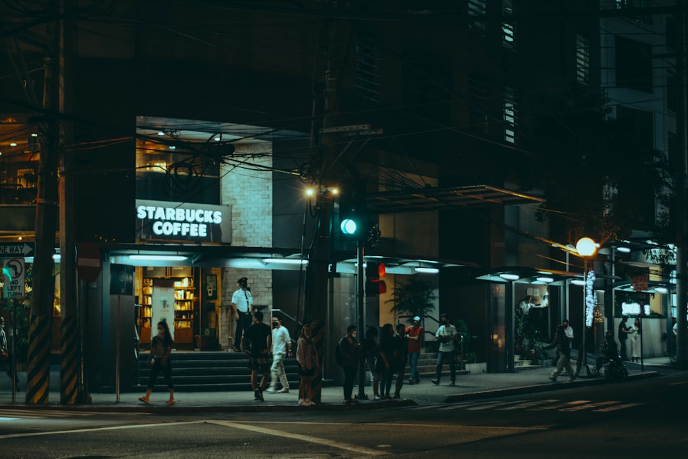 a group of people standing outside of a starbucks at night