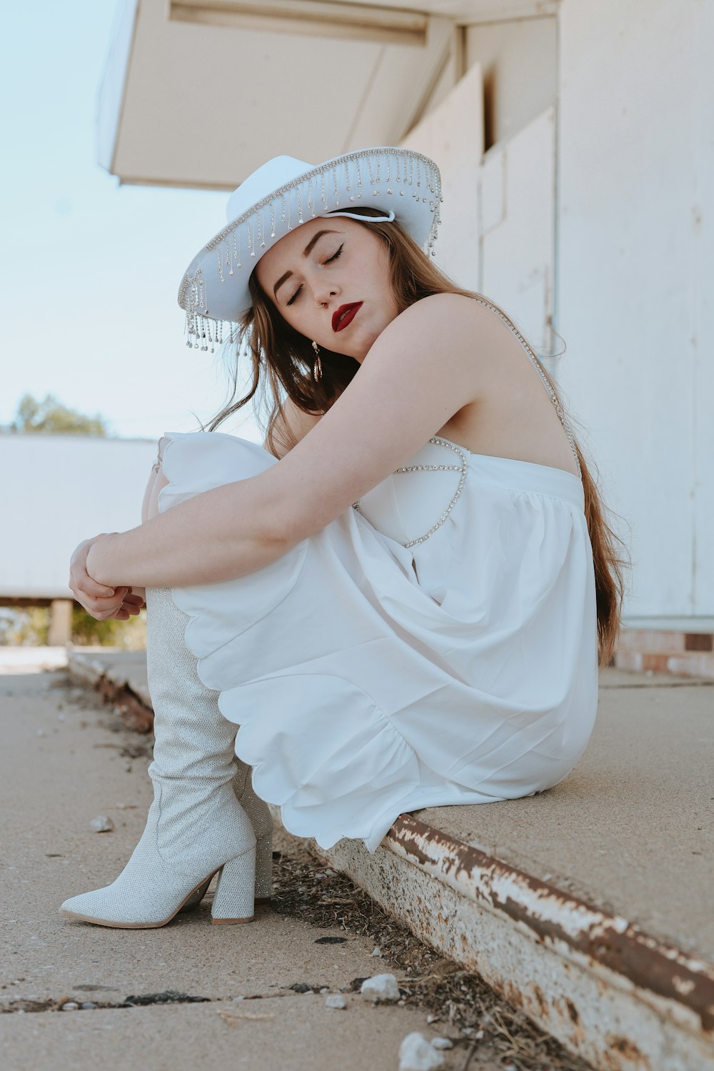 uma mulher de vestido branco e chapéu sentada no chão