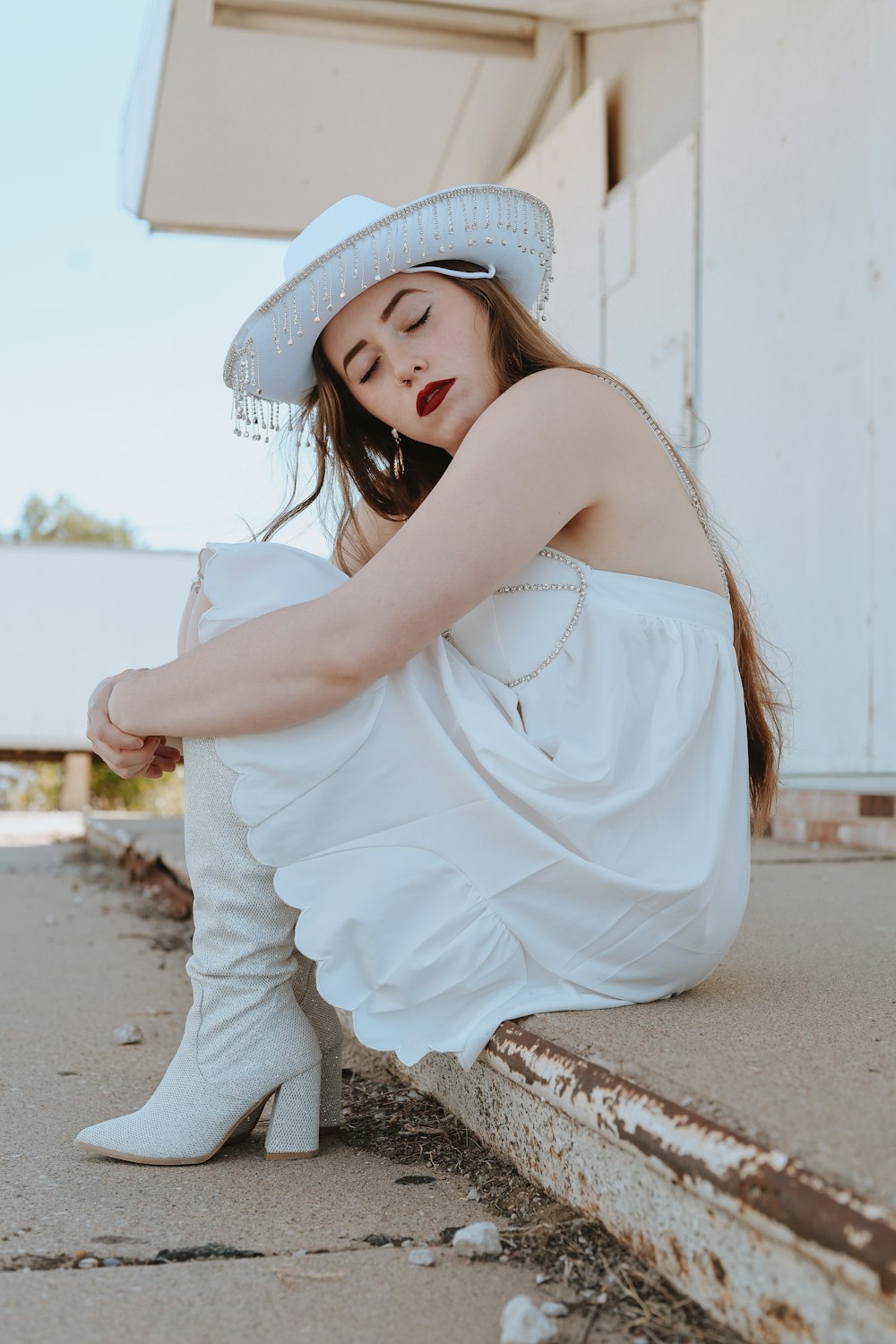 eine Frau in weißem Kleid und Hut, die auf dem Boden sitzt