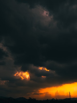 Dark storm clouds fill the sky, with patches of brilliant orange and yellow light breaking through near the horizon. The contrast between the ominous clouds and the warm light creates a dramatic and striking scene.